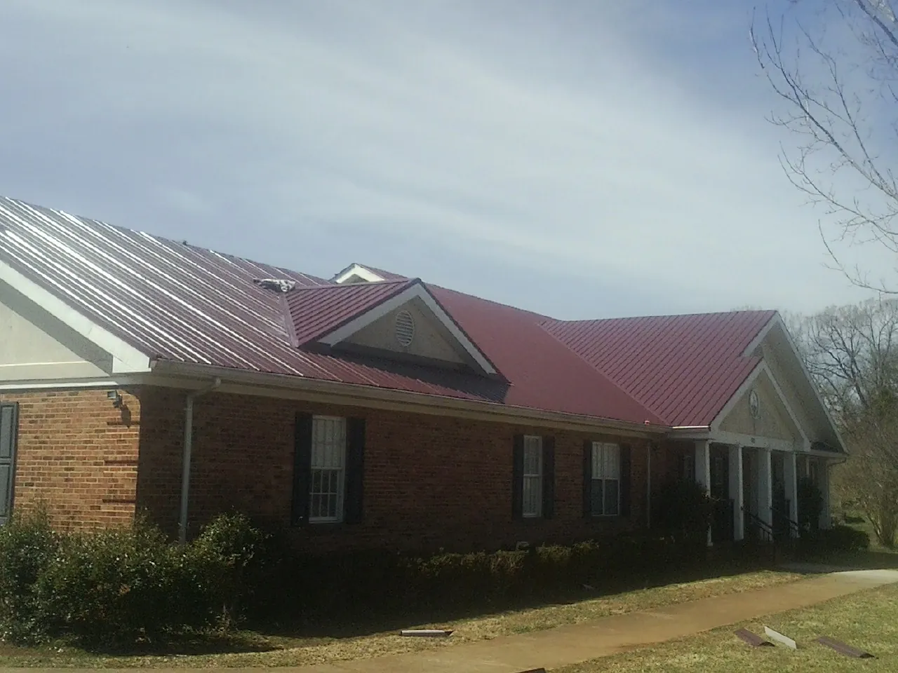 Red metal roof with gabled entries on a long brick building, from a Hail Damage Roof Repair job in Deal Island