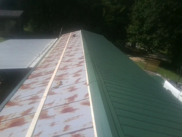 Old rusted panels beside newly installed green metal roofing — Wind Damage Roof Repair by Roofing Brothers in Deal Island