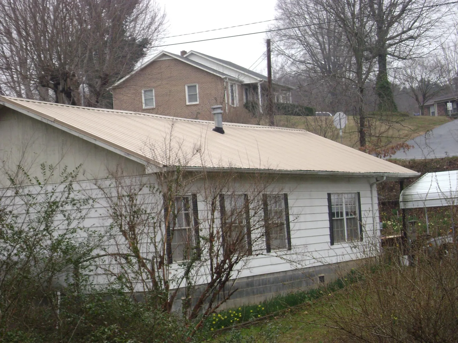Tan metal roof on a white sided house set into a hillside — Commercial Roofing by Roofing Brothers in Deal Island
